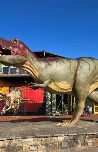 Ein lebensgroßes Dinosauriermodell steht vor einem roten Gebäude im Dinopark Münchehagen.A life-size dinosaur model stands in front of a red building in Dinopark Münchehagen.En dinosaurmodel i naturlig størrelse står foran en rød bygning i Dinopark Münchehagen.Een levensgroot dinosaurusmodel staat voor een rood gebouw in Dinopark Münchehagen.