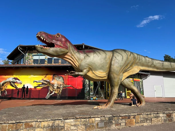 A life-size dinosaur model stands in front of a red building in Dinopark Münchehagen.