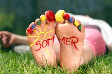 Spielen_im_Park.jpg Barfuß im Gras mit bunten Zehen, auf den Fußsohlen steht das Wort Sommer neben einer Sonne.