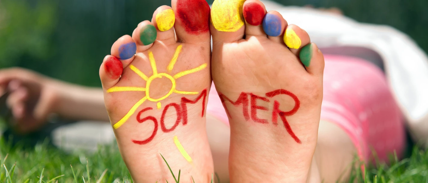 Spielen_im_Park.jpg Barfuß im Gras mit bunten Zehen, auf den Fußsohlen steht das Wort Sommer neben einer Sonne.