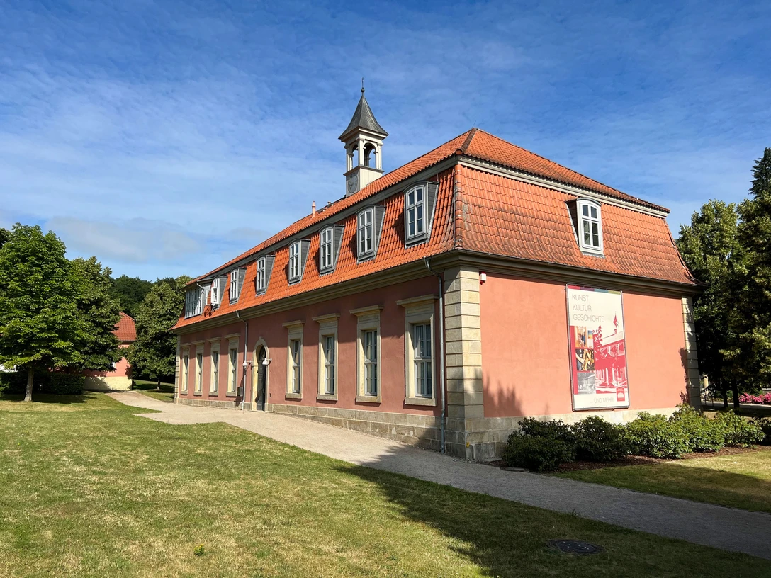 Klassizistisches Gebäude mit rotem Mansarddach und Turmspitze, am Waldrand von Bad Rehburg gelegen.