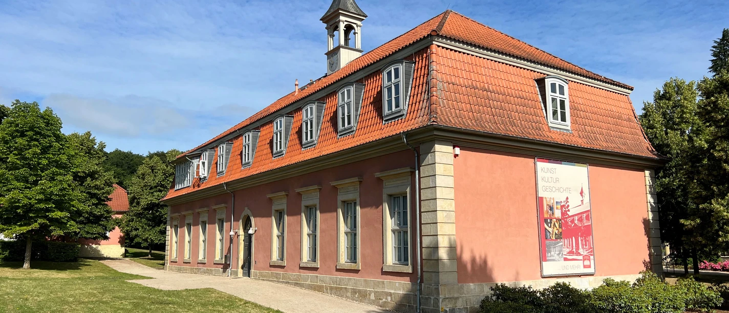 Klassizistisches Gebäude mit rotem Mansarddach und Turmspitze, am Waldrand von Bad Rehburg gelegen.