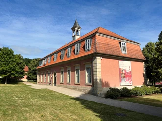 Romantik-Bad-Rehburg.jpg Klassizistisches Gebäude mit rotem Mansarddach und Turmspitze, am Waldrand von Bad Rehburg gelegen.