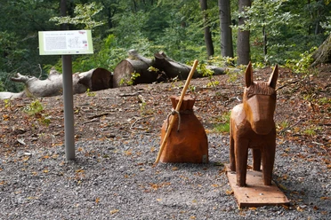 Holzfiguren von Esel und Beutel des Märchens Tischlein deck dich im bewaldeten Bereich am Wegesrand.