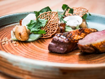 genussatelier-dresden-7.JPG Kunstvoll angerichtete Speisen mit Fleisch, Pilzen und dekorativen Elementen auf einem Keramikteller.