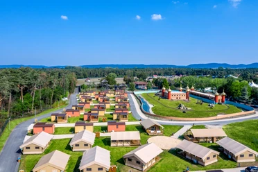 Luftaufnahme eines weitläufigen Erlebnisresorts mit Zelten, Grünflächen und einer Wasseranlage im Zentrum.