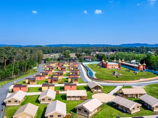 Luftaufnahme eines weitläufigen Erlebnisresorts mit Zelten, Grünflächen und einer Wasseranlage im Zentrum.