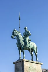 Cuirassier monument Bronze statue of a cuirassier on horseback on a high pedestal, with a lance above the blue sky.