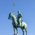 Cuirassier monument Bronzestatue eines Kürassiers zu Pferd auf einem hohen Sockel, mit einer Lanze über dem blauen Himmel. Bronze statue of a cuirassier on horseback on a high pedestal, with a lance above the blue sky.