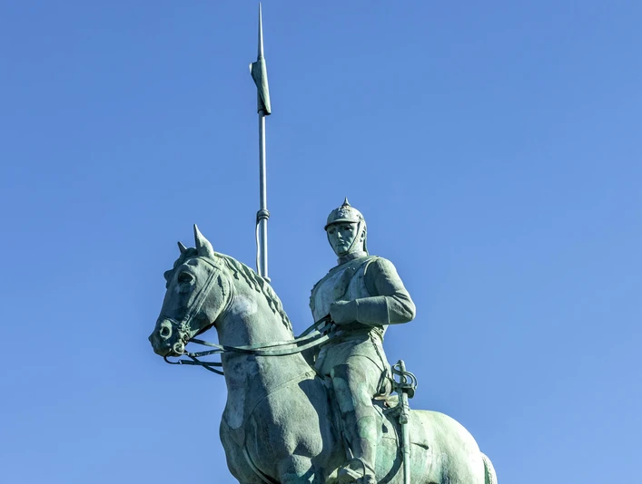 Cuirassier monument Bronzestatue eines Kürassiers zu Pferd auf einem hohen Sockel, mit einer Lanze über dem blauen Himmel. Bronze statue of a cuirassier on horseback on a high pedestal, with a lance above the blue sky.