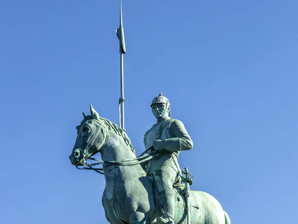 Kuerassierdenkmal Bronzestatue eines Kürassiers zu Pferd auf einem hohen Sockel, mit einer Lanze über dem blauen Himmel.