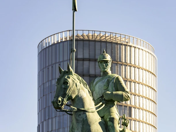 Cuirassier monument A statue of a cuirassier on horseback, with a modern round tower in the background.