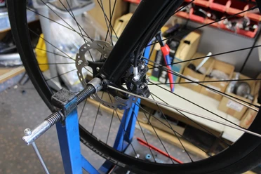 Radreparatur Ein Fahrrad wird auf einem blauen Halter für Wartungsarbeiten fixiert, Werkzeug ist im Hintergrund sichtbar.