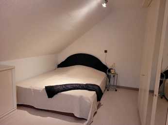 Dachgeschosszimmer mit Doppelbett, schlichtem Design und kleinem Nachttisch mit Leselampe.