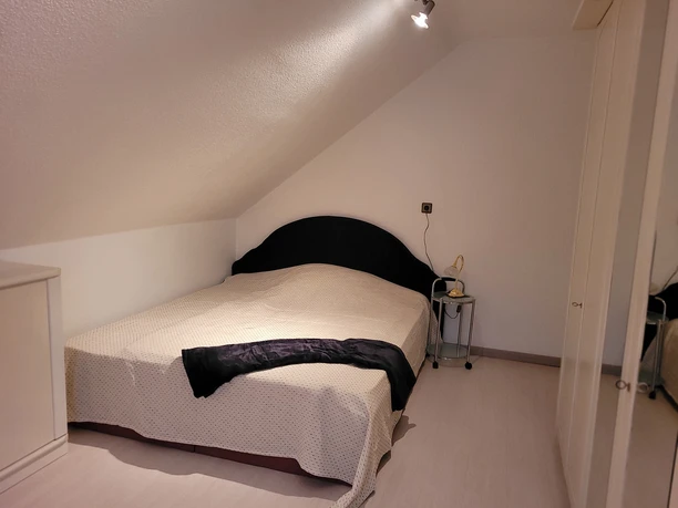 Dachgeschosszimmer mit Doppelbett, schlichtem Design und kleinem Nachttisch mit Leselampe.