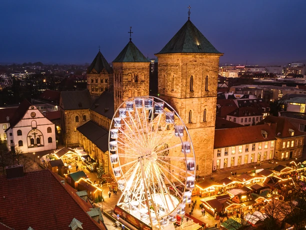 Osnabrücker Weihnachtsmarkt bei Abenddämmerung, beleuchtetes Riesenrad vor historischen Gebäuden.