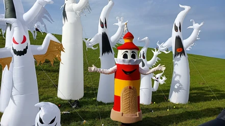 Lükko Leuchtturm beim Drachenfest in Upleward am Deich Die Figur Lükko Leuchtturm steht inmitten von Drachen-Geisterfiguren bei Sonnenschein auf dem Deich.