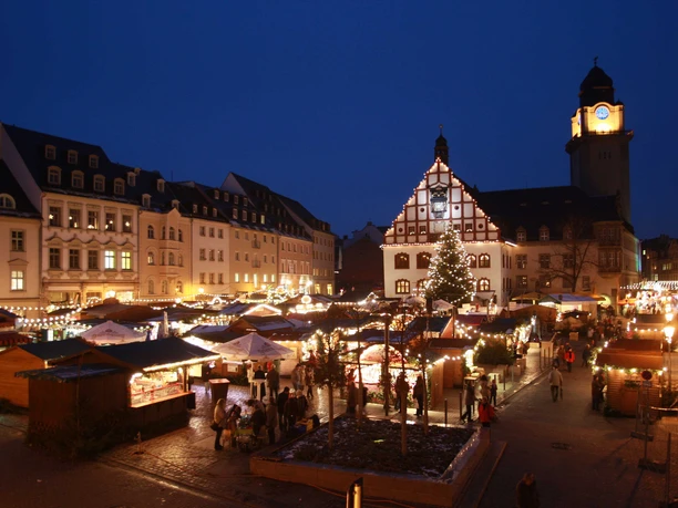 Plauen_Stadtverwaltung Plauen.jpg Festlich beleuchteter Weihnachtsmarkt vor historischem Gebäude bei Abenddämmerung.