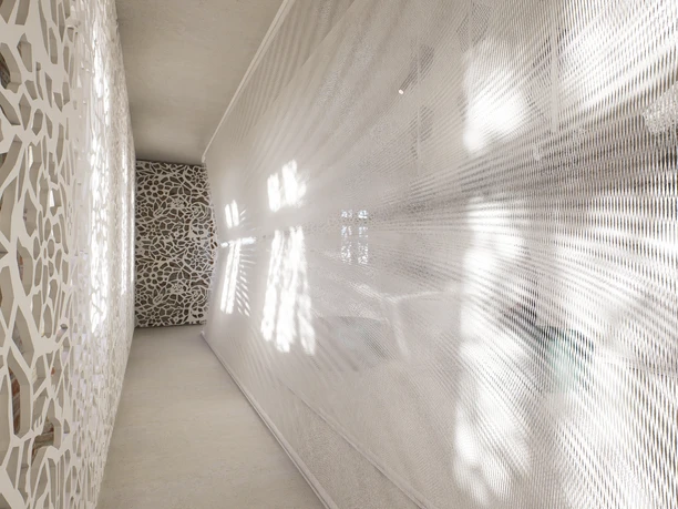 D5_Image_20221228_160857.png Ein langer, schmaler Raum mit weißem, geometrischem Muster an den Wänden und lichtdurchflutetem Stoff.