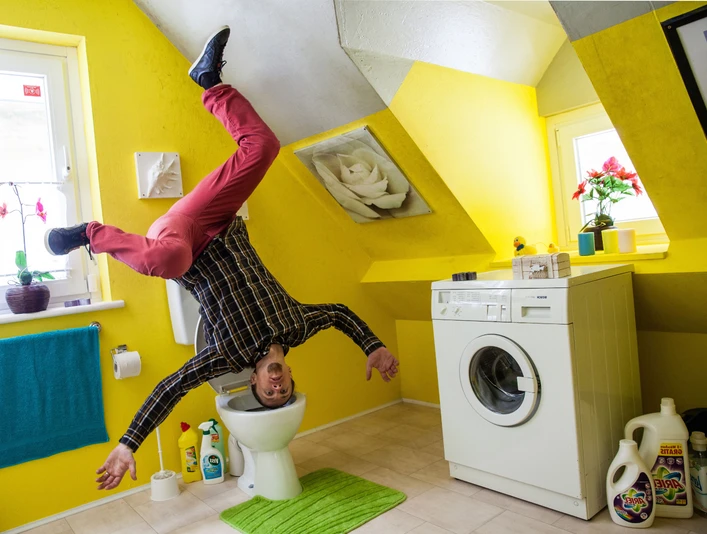das-verrueckte-haus.jpg Das Bild zeigt einen Mann, der freudig in einem Raum steht, dessen Einrichtung kopfüber an der Decke angebracht ist. Zu sehen sind eine Waschmaschine, ein WC und bunte Wände in einem surrealen, umgekehrten Haus.The picture shows a man standing joyfully in a room whose furnishings are upside down on the ceiling. You can see a washing machine, a toilet and colorful walls in a surreal, upside-down house.Billedet viser en mand, der står glad i et rum, hvis møbler er monteret på hovedet i loftet. En vaskemaskine, et toilet og farverige vægge ses i et surrealistisk hus, der er vendt på hovedet.Op de foto staat een man vrolijk in een kamer waarvan de meubels ondersteboven aan het plafond zijn bevestigd. Een wasmachine, een toilet en kleurrijke muren zijn te zien in een surrealistisch, ondersteboven huis.