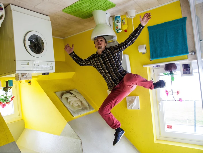 das-verrueckte-haus.jpg Das Bild zeigt einen Mann, der freudig in einem Raum steht, dessen Einrichtung kopfüber an der Decke angebracht ist. Zu sehen sind eine Waschmaschine, ein WC und bunte Wände in einem surrealen, umgekehrten Haus.The picture shows a man standing joyfully in a room whose furnishings are upside down on the ceiling. You can see a washing machine, a toilet and colorful walls in a surreal, upside-down house.Billedet viser en mand, der står glad i et rum, hvis møbler er monteret på hovedet i loftet. En vaskemaskine, et toilet og farverige vægge ses i et surrealistisk hus, der er vendt på hovedet.Op de foto staat een man vrolijk in een kamer waarvan de meubels ondersteboven aan het plafond zijn bevestigd. Een wasmachine, een toilet en kleurrijke muren zijn te zien in een surrealistisch, ondersteboven huis.
