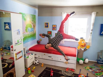 das-verrueckte-haus-balanceakt (1).jpg Ein Mann steht auf der Decke eines bunt gestalteten Kinderzimmers, als befände er sich in einem verkehrten Raum.A man stands on the ceiling of a colorful children's room as if he were in an upside-down room.En mand står på loftet i et farverigt designet børneværelse, som om han var i et rum, der var vendt på hovedet.Een man staat op het plafond van een kleurrijk ontworpen kinderkamer alsof hij zich in een omgekeerde kamer bevindt.