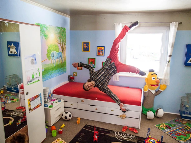 das-verrueckte-haus-balanceakt (1).jpg A man stands on the ceiling of a colorful children's room as if he were in an upside-down room.