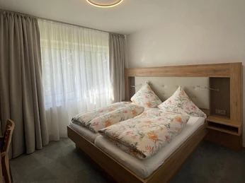 Zimmer Doppelbett im modernen Zimmer mit floral bedruckter Bettwäsche, großem Fenster und Holzdetails.