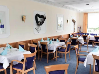 Saal Blau Ein elegantes Restaurant mit fein gedeckten Tischen, blauen Stühlen und moderner Wanddekoration.