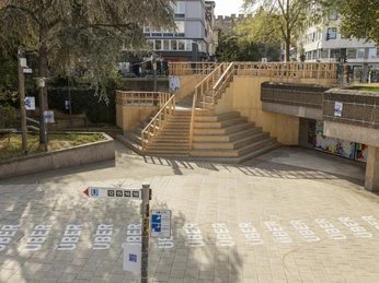 Ebertplatz Im Zentrum von Köln befindet sich der städtische Ebertplatz, umgeben von modernen Gebäuden und Bäumen. Eine helle, großzügige Treppenanlage führt zur erhöhten Plattform, die Sitzgelegenheiten bietet. Pflastersteine und Wegweiser prägen den Platz, der durch seine Klarheit und Zugänglichkeit besticht.The municipal Ebertplatz is located in the center of Cologne, surrounded by modern buildings and trees. A bright, spacious staircase leads to the raised platform, which offers seating. Paving stones and signposts characterize the square, which impresses with its clarity and accessibility.