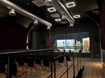 Heimatscheune Martfeld Das Foto zeigt den Innenraum der Heimatscheune Martfeld mit Bühne, schwarzen Vorhängen und Stuhlreihen.