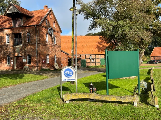 Ziegelbauernhof mit roten Dächern, vorne ein Fahrradschild für Lufttanken, im grünen Umfeld.