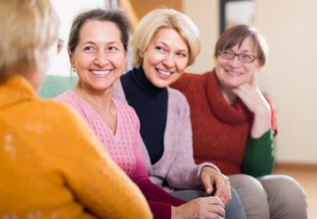 OFT_©_AdobeStock_75781536_JackF.jpg Vier lächelnde Frauen mittleren Alters sitzen in einem Gesprächskreis in einem Wohnzimmer.
