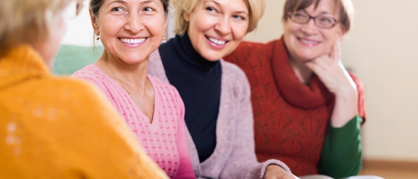 OFT_©_AdobeStock_75781536_JackF.jpg Vier lächelnde Frauen mittleren Alters sitzen in einem Gesprächskreis in einem Wohnzimmer.