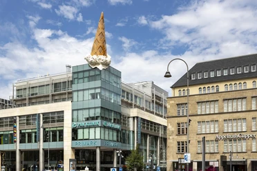 Skulptur Dropped Cone von Claes Oldenburg und Coosje van Bruggen am Kölner Neumarkt Ein großes Gebäude in Köln wird von einer überdimensionalen, kopfüber stehenden Eiswaffel geschmückt, ein berühmtes Kunstwerk namens "Dropped Cone".