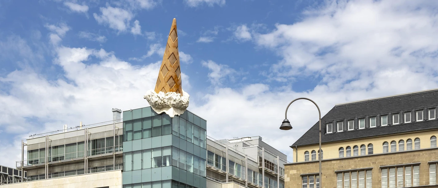 Skulptur Dropped Cone von Claes Oldenburg und Coosje van Bruggen am Kölner Neumarkt Ein großes Gebäude in Köln wird von einer überdimensionalen, kopfüber stehenden Eiswaffel geschmückt, ein berühmtes Kunstwerk namens "Dropped Cone".