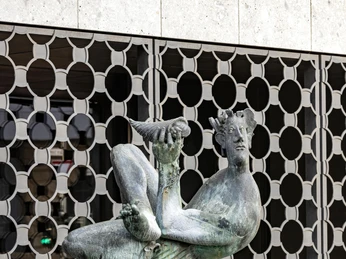 Dionysus Fountain Die Bronzestatue des Dionysos-Brunnens in Köln zeigt eine mythologische Figur, die lässig auf einem Sockel sitzt und eine Schale hebt.The bronze statue of the Dionysus Fountain in Cologne shows a mythological figure sitting casually on a pedestal and lifting a bowl.