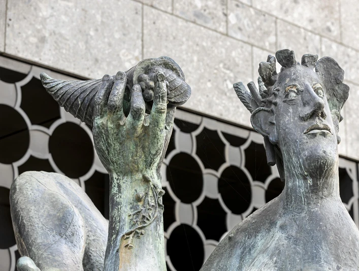 Dionysus Fountain Bronzestatue des Dionysos an einem Brunnen in Köln, hält fröhlich eine Muschel in der Hand, kunstvoll gestaltet gegen modernen Steinbau. Die detaillierten Gesichtszüge und die mächtige Muschel verleihen dem Ensemble einen besonderen Charme.Bronze statue of Dionysus at a fountain in Cologne, cheerfully holding a shell in his hand, artistically designed against a modern stone structure. The detailed facial features and the mighty shell lend the ensemble a special charm.