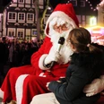 1.jpg Weihnachtsmann spricht lächelnd mit einem Kind, im Hintergrund festlich geschmückte Fachwerkhäuser.