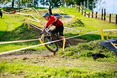 MTB-Rundkurs Ein Mountainbiker in rotem Trikot fährt dynamisch durch einen grasigen, abgesperrten Parcours.