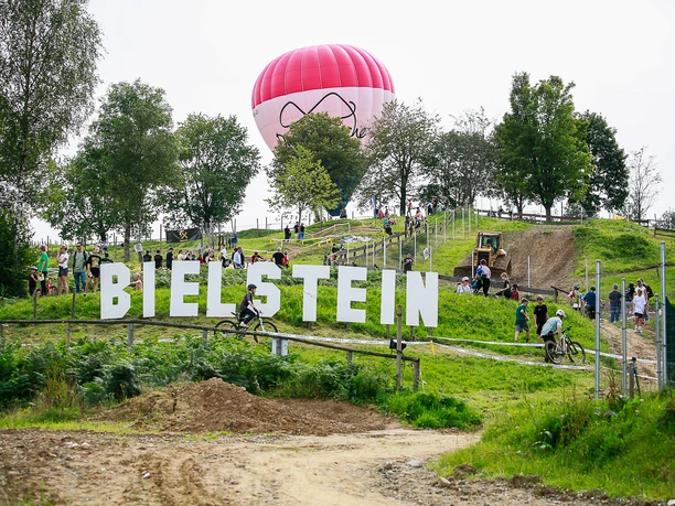 MTB-Rundkurs Fahrradfahrer im grünen Gelände von Bielstein, im Hintergrund ein großer roter Heißluftballon.