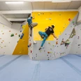 Zwei Personen klettern in einer hellen, modernen Kletterhalle mit farbigen Griffen an der Wand.