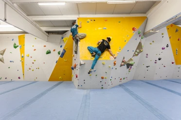 Paderborn Kletterhalle Zwei Personen klettern in einer hellen, modernen Kletterhalle mit farbigen Griffen an der Wand.