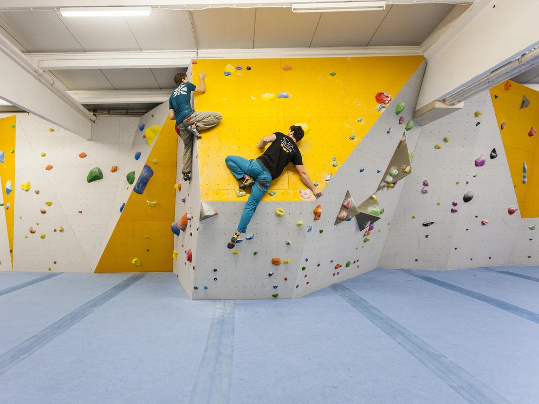 Paderborn Kletterhalle Zwei Personen klettern in einer hellen, modernen Kletterhalle mit farbigen Griffen an der Wand.