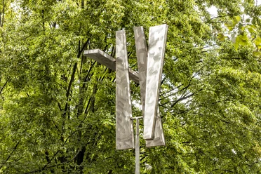 Four Trapezoids as two Rectangles IV Eine moderne Skulptur aus Aluminium-Trapezen erhebt sich vor dichtem grünen Laub.