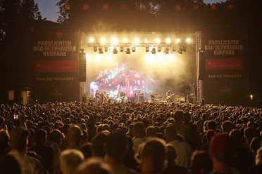 Der Parklichter-Freitag Klar! Hier ist eine überarbeitete VersioDas Bild zeigt den Parklichter Freitag, bei dem das Konzert gerade seinen Höhepunkt erreicht hat. Eine große Menschenmenge versammelt sich vor der Bühne und genießt die mitreißende Musik.