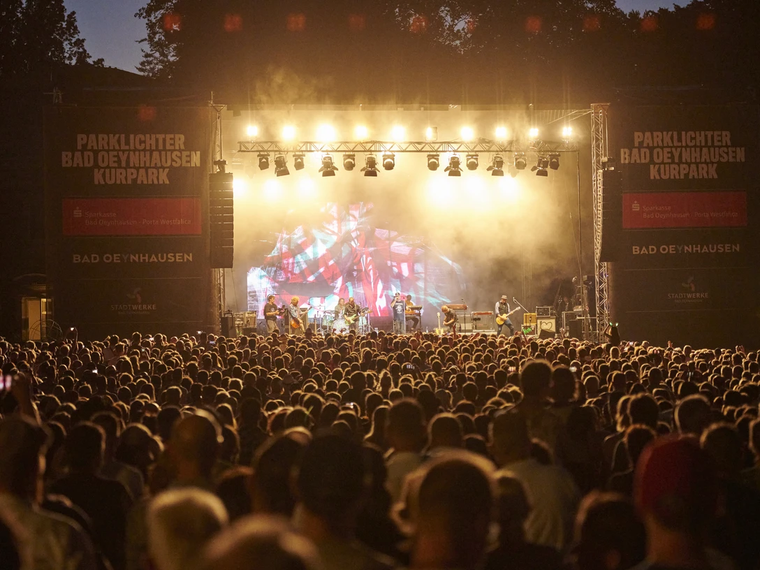 Der Parklichter-Freitag Klar! Hier ist eine überarbeitete VersioDas Bild zeigt den Parklichter Freitag, bei dem das Konzert gerade seinen Höhepunkt erreicht hat. Eine große Menschenmenge versammelt sich vor der Bühne und genießt die mitreißende Musik.