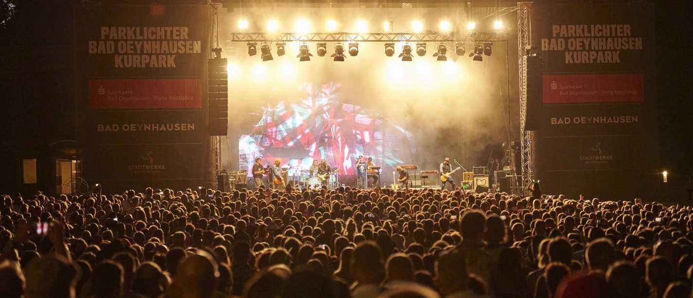 Der Parklichter-Freitag Klar! Hier ist eine überarbeitete VersioDas Bild zeigt den Parklichter Freitag, bei dem das Konzert gerade seinen Höhepunkt erreicht hat. Eine große Menschenmenge versammelt sich vor der Bühne und genießt die mitreißende Musik.