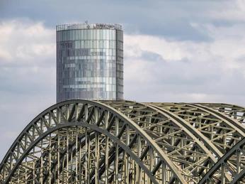 KölnTriangle Das Bild zeigt die Hohenzollernbrücke und den markanten KölnTriangle-Turm bei bewölktem Himmel.The picture shows the Hohenzollern Bridge and the striking Cologne Triangle Tower under a cloudy sky.