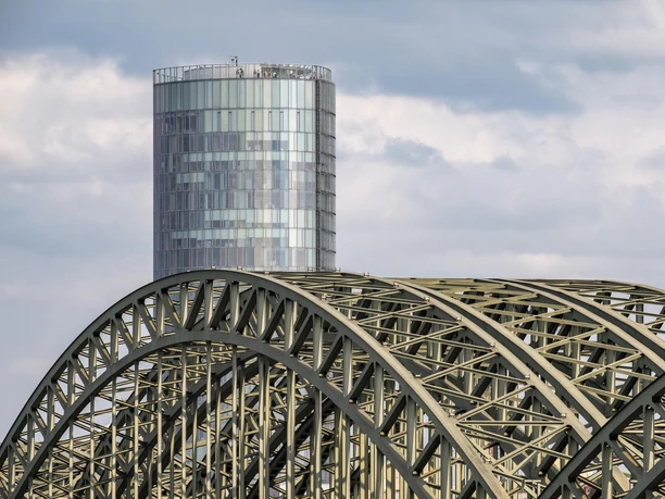 KölnTriangle The picture shows the Hohenzollern Bridge and the striking Cologne Triangle Tower under a cloudy sky.